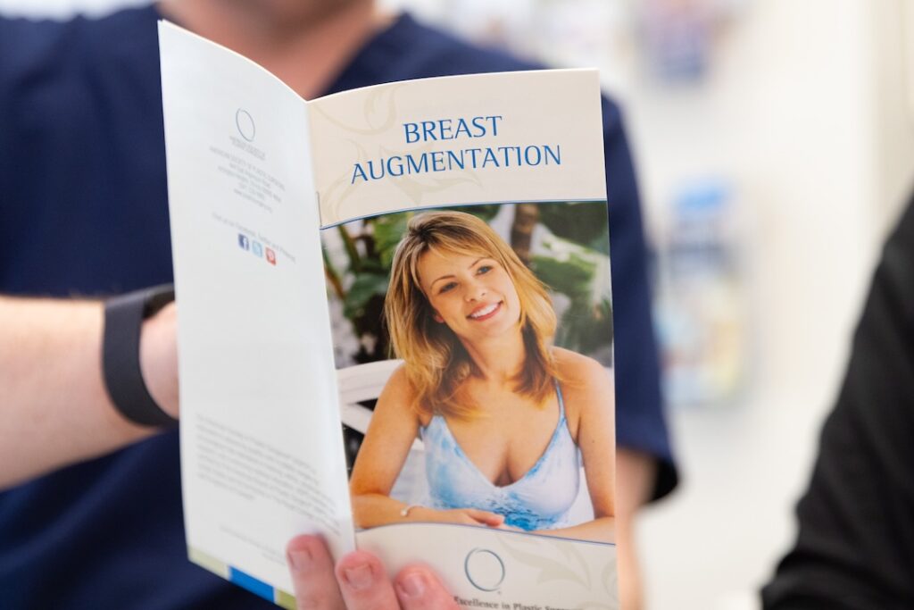 A brochure for breast aug near Bethesda, MD, with a middle-aged woman on the front in a strappy blue dress and blonde hair. A physician with a watch and navy scrubs on explains the options for surgery to their patient.